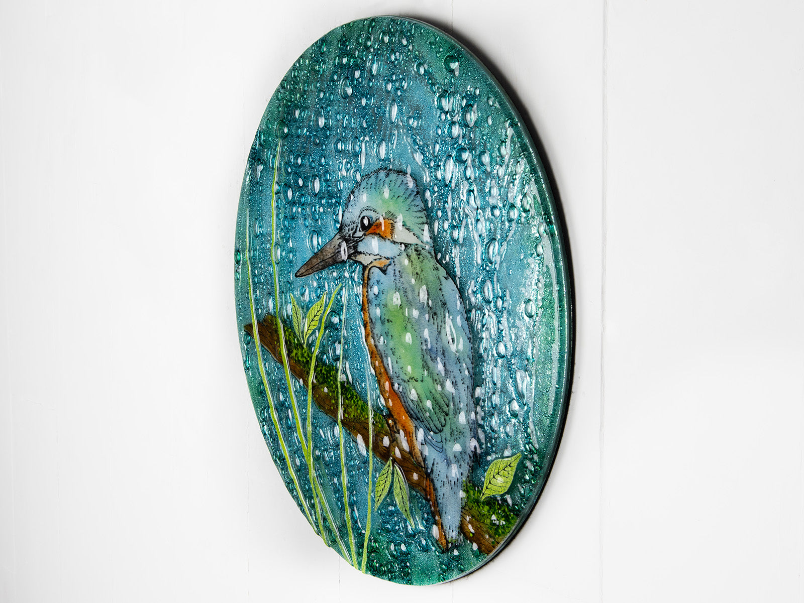 Side image of a round fused glass wall panel, with hand-painted kingfisher design in vibrant organic colours and textures. 