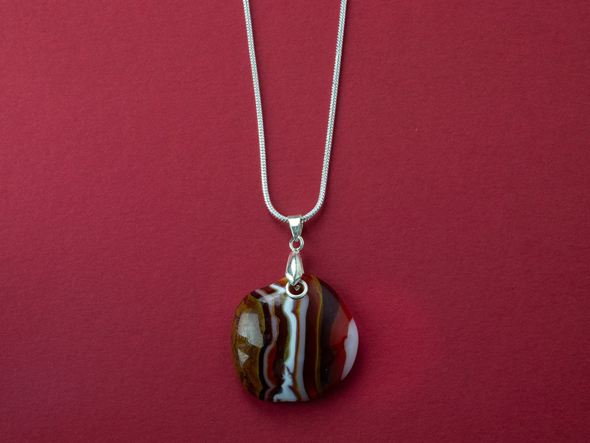 A sterling silver chain necklace with a fused glass pendant featuring a marbled pattern of bright reds and autumnal hues.