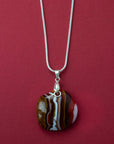 A sterling silver chain necklace with a fused glass pendant featuring a marbled pattern of bright reds and autumnal hues.