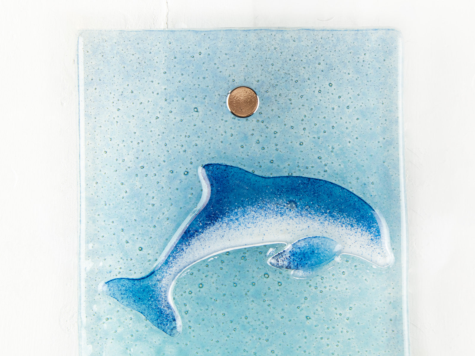 close up of fused glass dolphin on a marine blue wall panel.