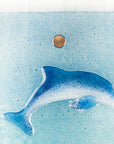 close up of fused glass dolphin on a marine blue wall panel.