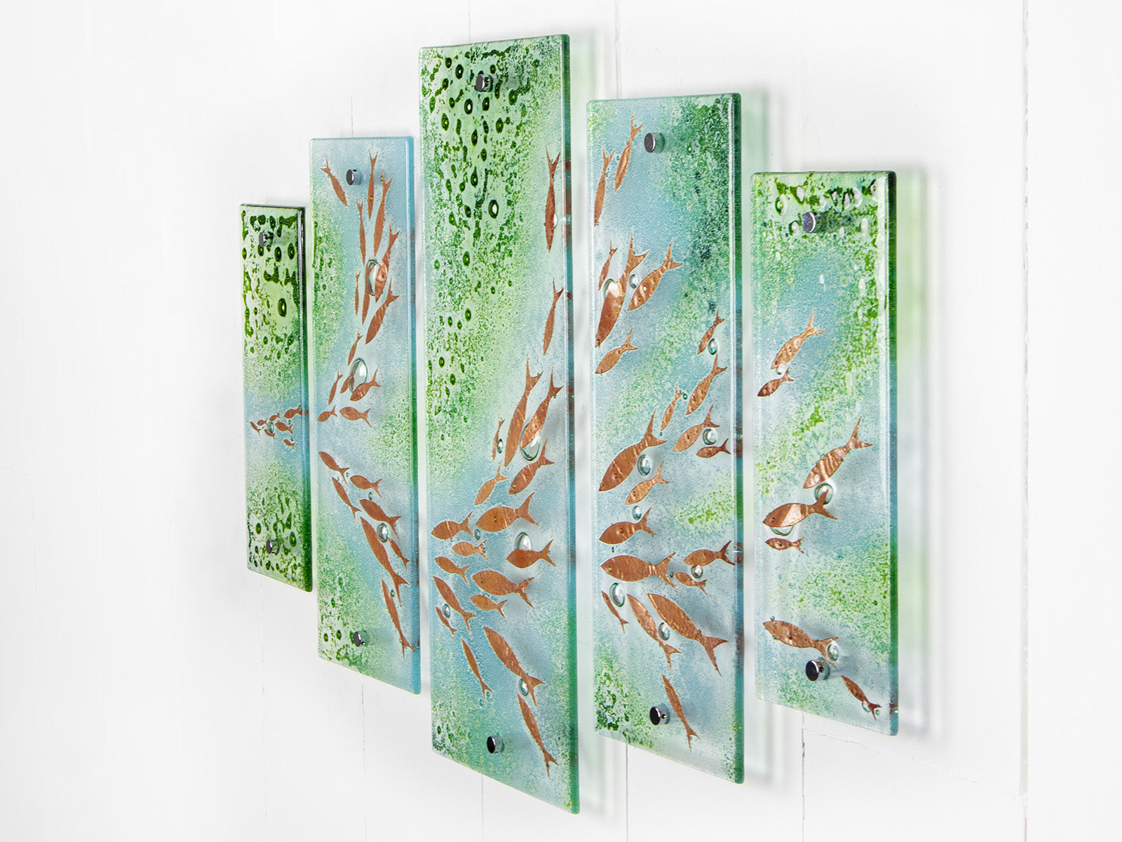 A fused glass quintych featuring a soft coastal colour-way with darting copper fish and bubbled detailing. An ocean inspired piece of wall art. 
