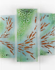 A fused glass quintych featuring a soft coastal colour-way with darting copper fish and bubbled detailing. An ocean inspired piece of wall art. 