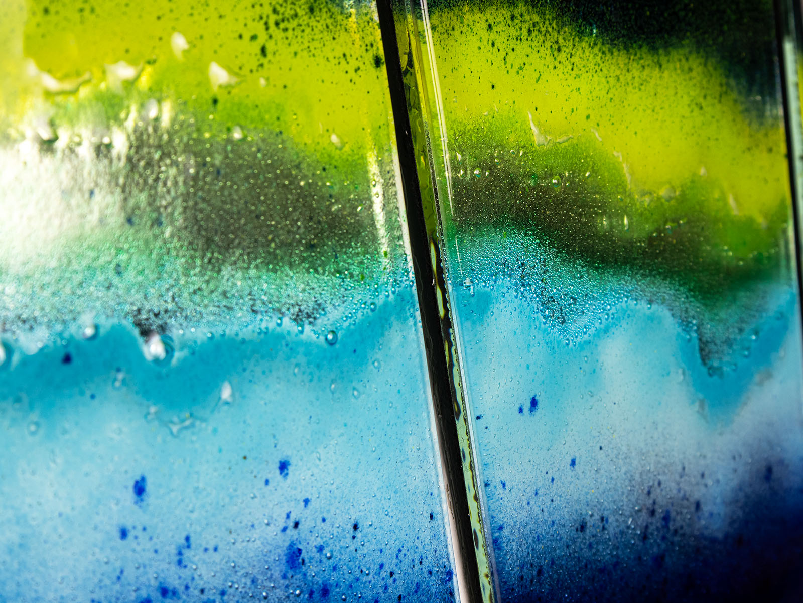 Close up of fused glass staggered triptych in bright rainbow colours, placed onto mirror glass. A vibrant piece of wall art. 