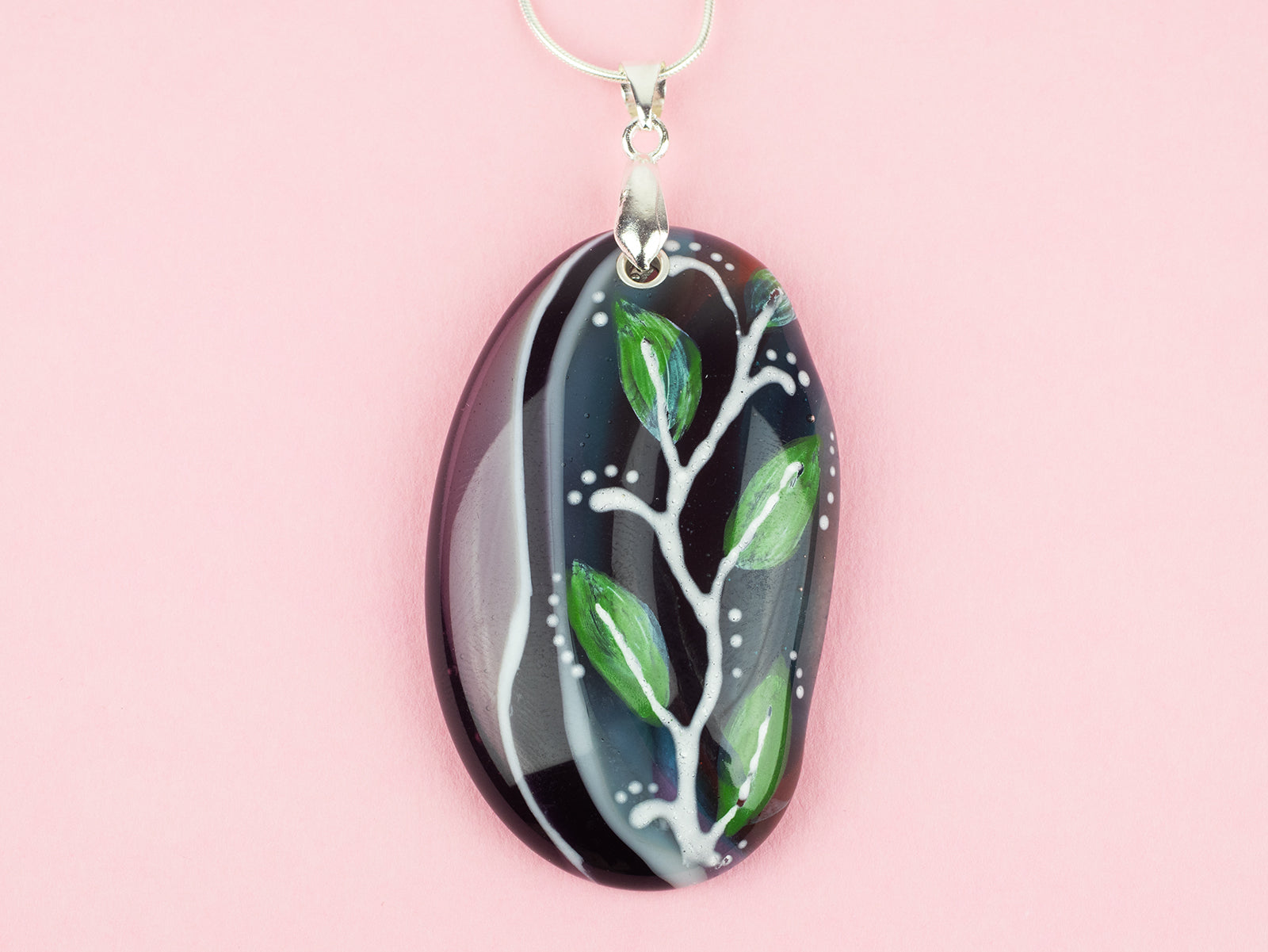 Close up of fused glass pendant necklace, handmade in spring greens and pinks, with botanical hand-painted design. 