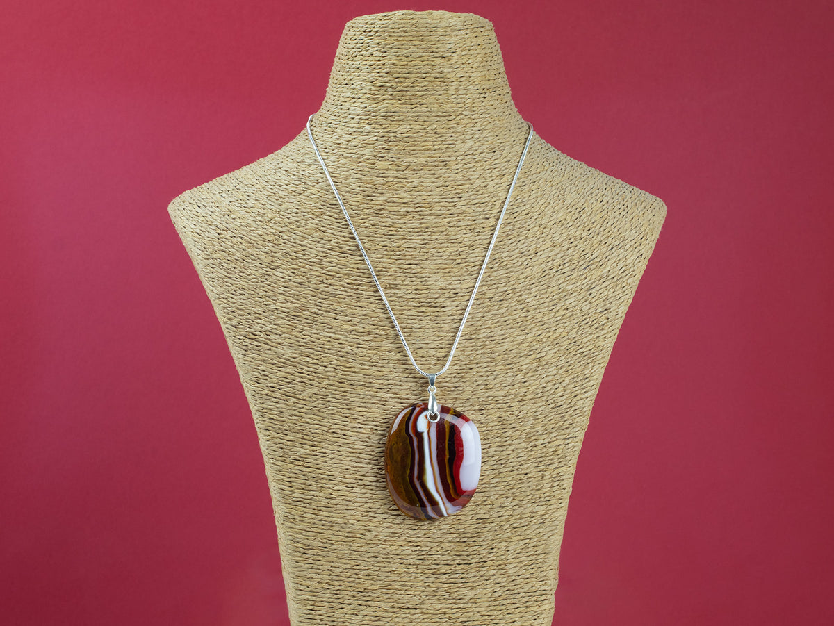 A sterling silver chain necklace with a fused glass pendant featuring a marbled pattern of reds and autumnal hues, seen on a mannequin. 