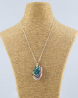 A fused glass pendant necklace on a sterling silver chain, handmade with soft coastal colours and a hint of red, with a hand-painted botanical design and a dichroic glass pebble. 