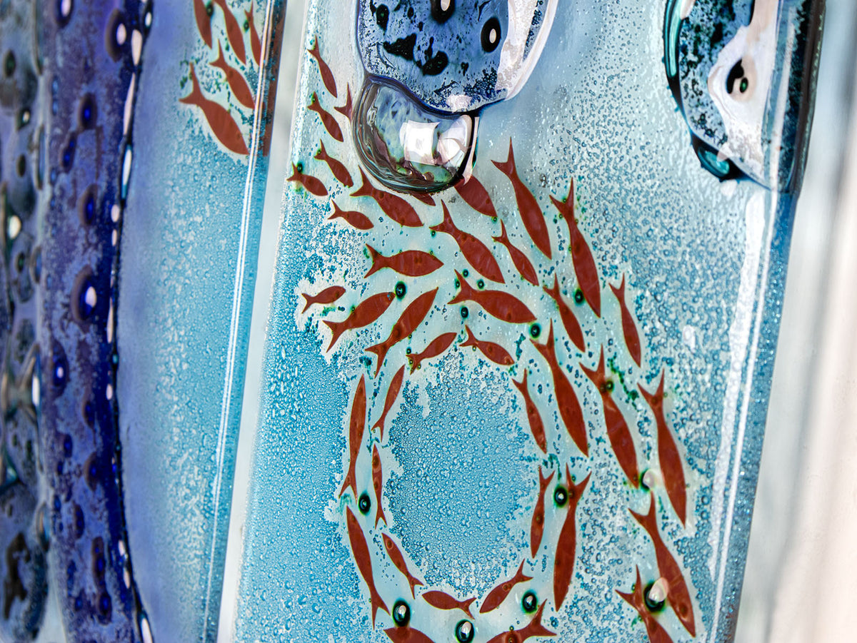 Details of the fish featured on a fused glass staggered triptych wall display, handmade in bright ocean blues and aquas, in a coastal rock-pool design, featuring copper fish. 
