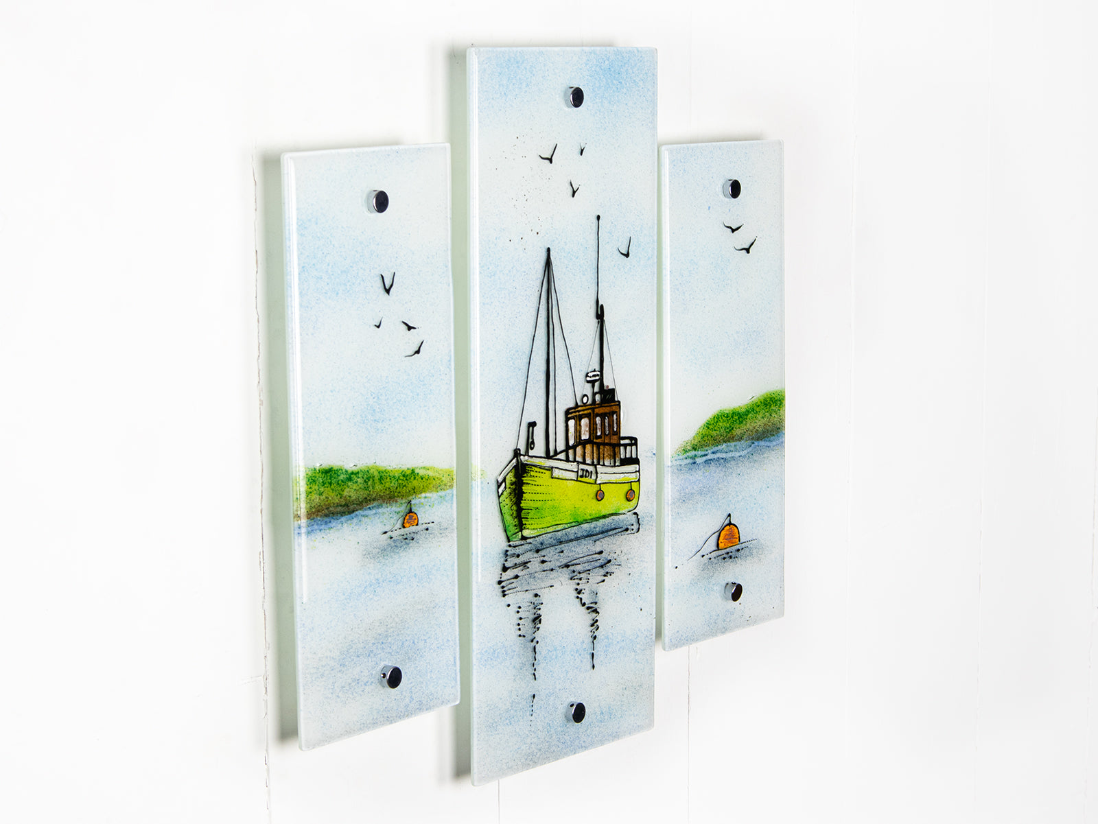 A side image of a staggered fused glass wall art triptych, with hand-painted fishing boat and a soft costal colour-way. 