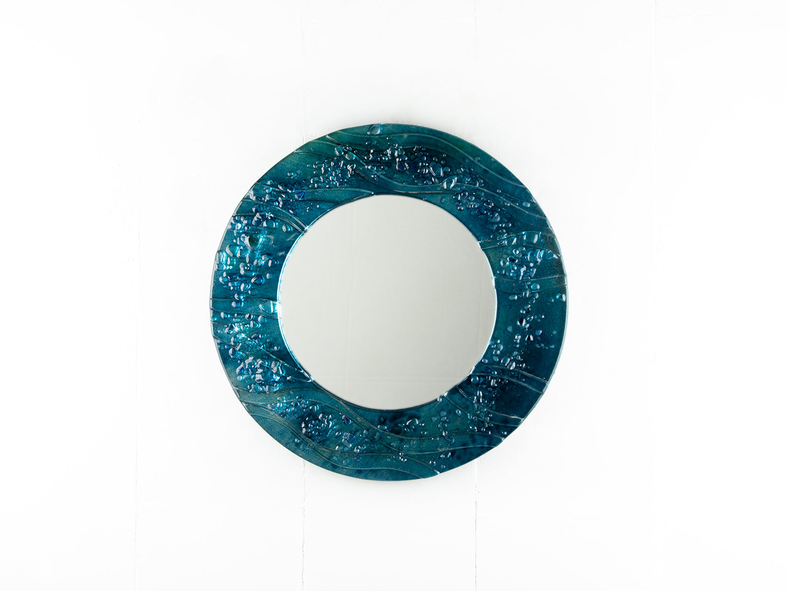 Circular fused glass mirror, featuring teal blue textured waves, creating a coastal and ocean inspired wall art design. 