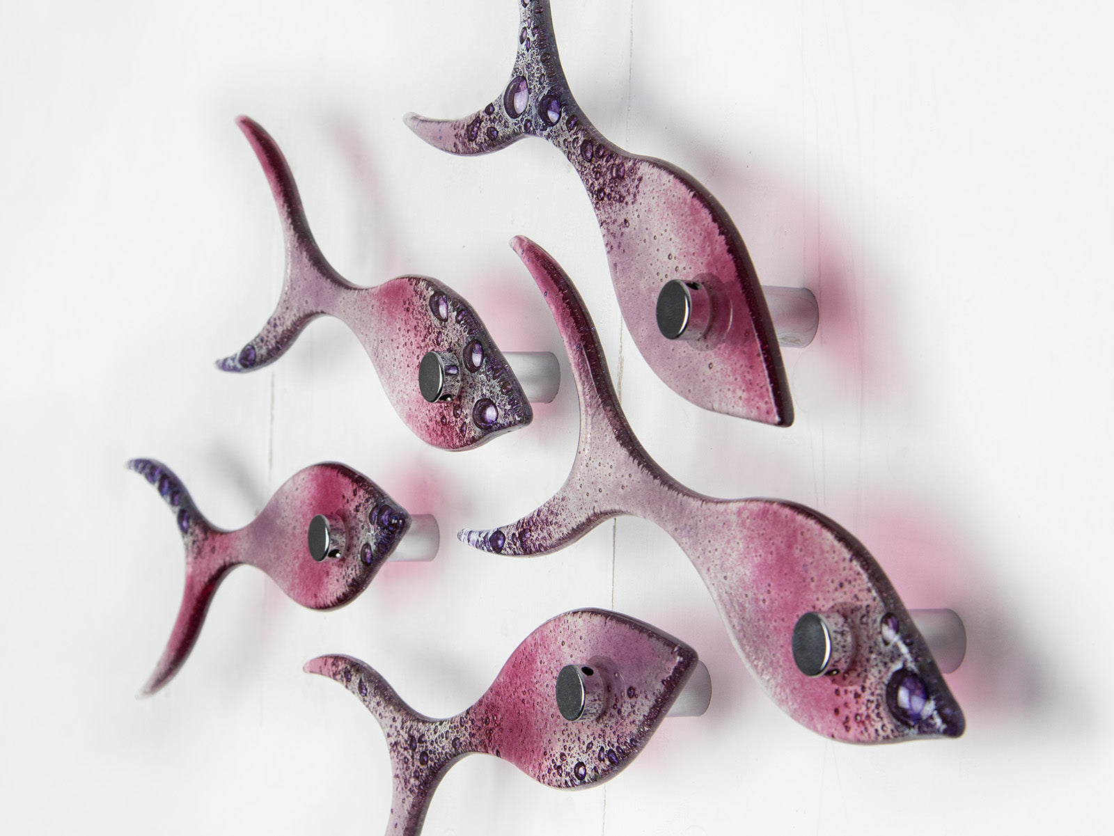 Side image of small fused glass wall display of individual handmade fish in rose pinks and bubbled purple hues. 