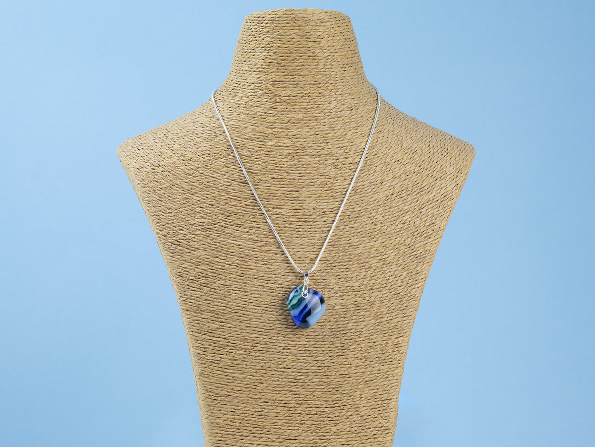 A sterling silver chain necklace with a round fused glass pendant featuring an aqua, blue design, handmade in coastal colours, seen on a mannequin 