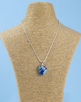 A sterling silver chain necklace with a round fused glass pendant featuring an aqua, blue design, handmade in coastal colours, seen on a mannequin 