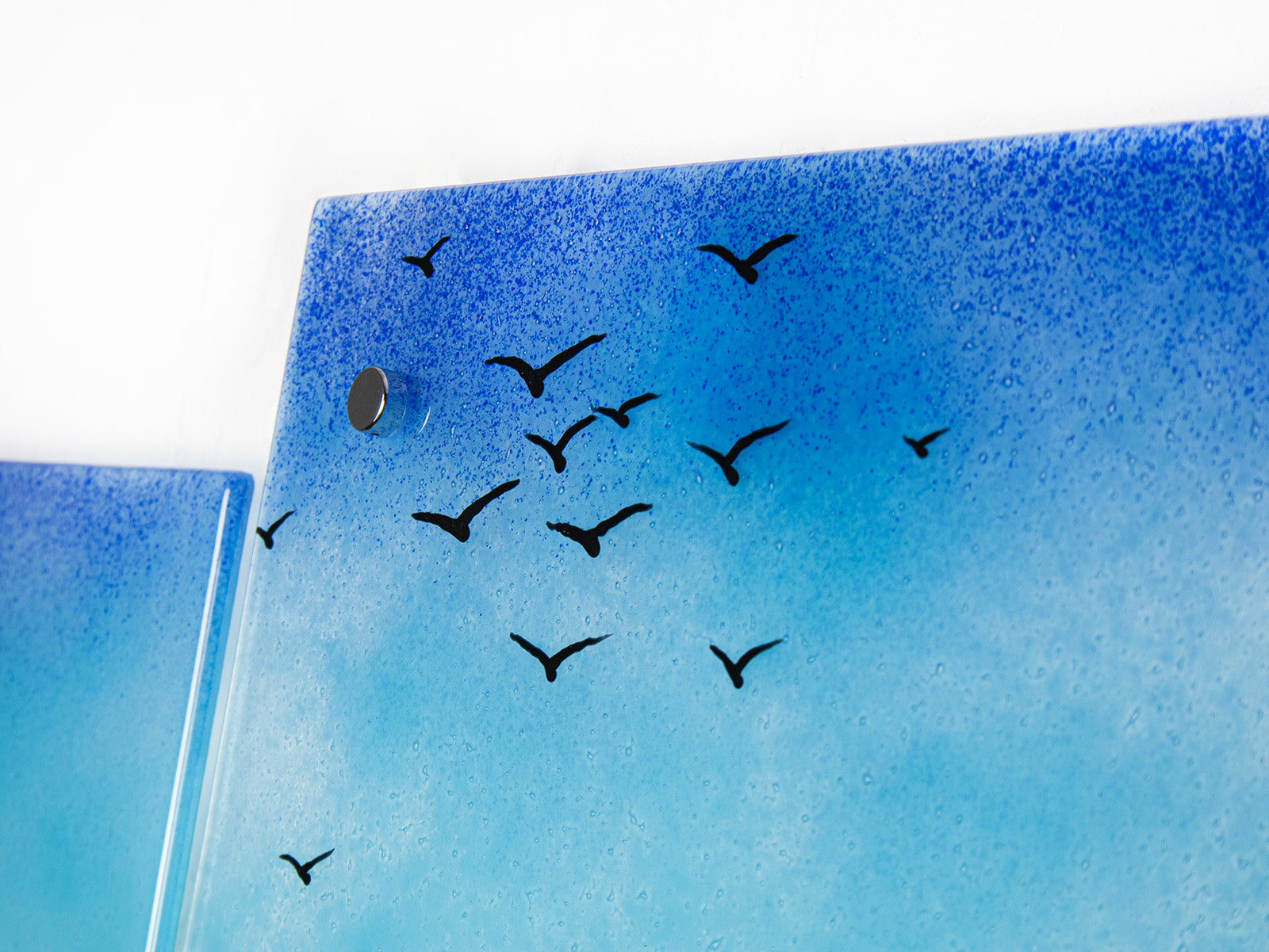 Close up of distant soaring sea birds on a fused glass triptych in coastal colours, with a lighthouse sat on a cliff and a Cornish tin mine. Hand-made coastal wall art, with texture. 