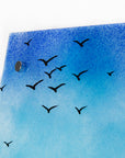 Close up of distant soaring sea birds on a fused glass triptych in coastal colours, with a lighthouse sat on a cliff and a Cornish tin mine. Hand-made coastal wall art, with texture. 