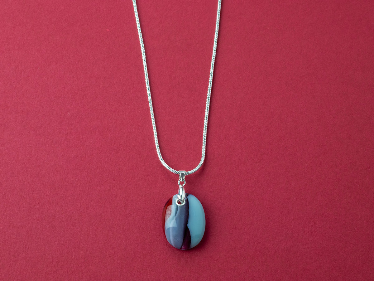 Artisan fused glass pendant necklace, handcrafted in our studio, with delicate blues and a flash of bright red. Finished with a sterling silver chain and fittings, a striking piece of wearable art