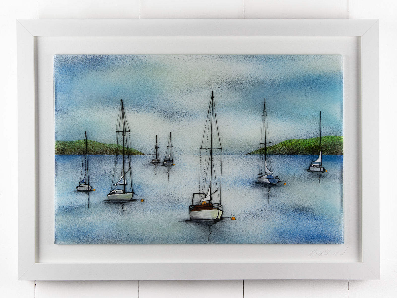 A hand-painted fused glass design of several sailboats anchored, designed in soft coastal colours and presented in a white frame.