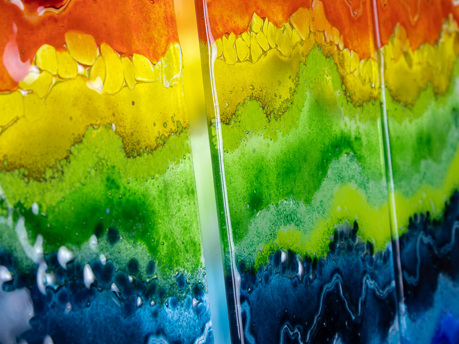 Close up of a fused glass wall art piece featuring wavy horizontal rainbow stripes in red, orange, yellow, green, blue, and purple.
