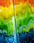 Close up of a fused glass wall art piece featuring wavy horizontal rainbow stripes in red, orange, yellow, green, blue, and purple.