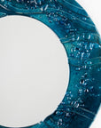 Close up of circular fused glass mirror, featuring teal blue textured waves, creating a coastal and ocean inspired wall art design. 