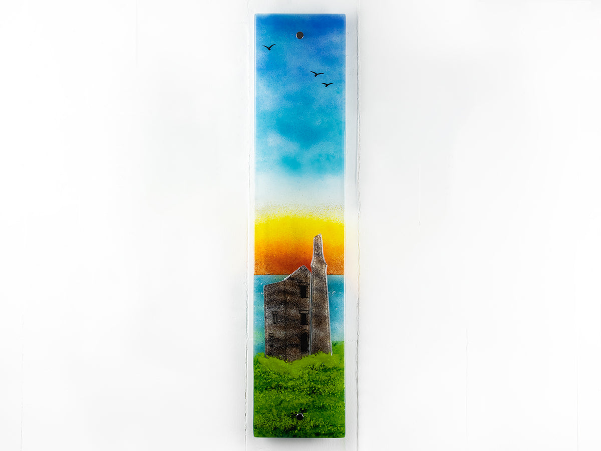 Fused glass wall panel, featuring a tin mine design, set against a vibrant sunrise in coastal colours. 