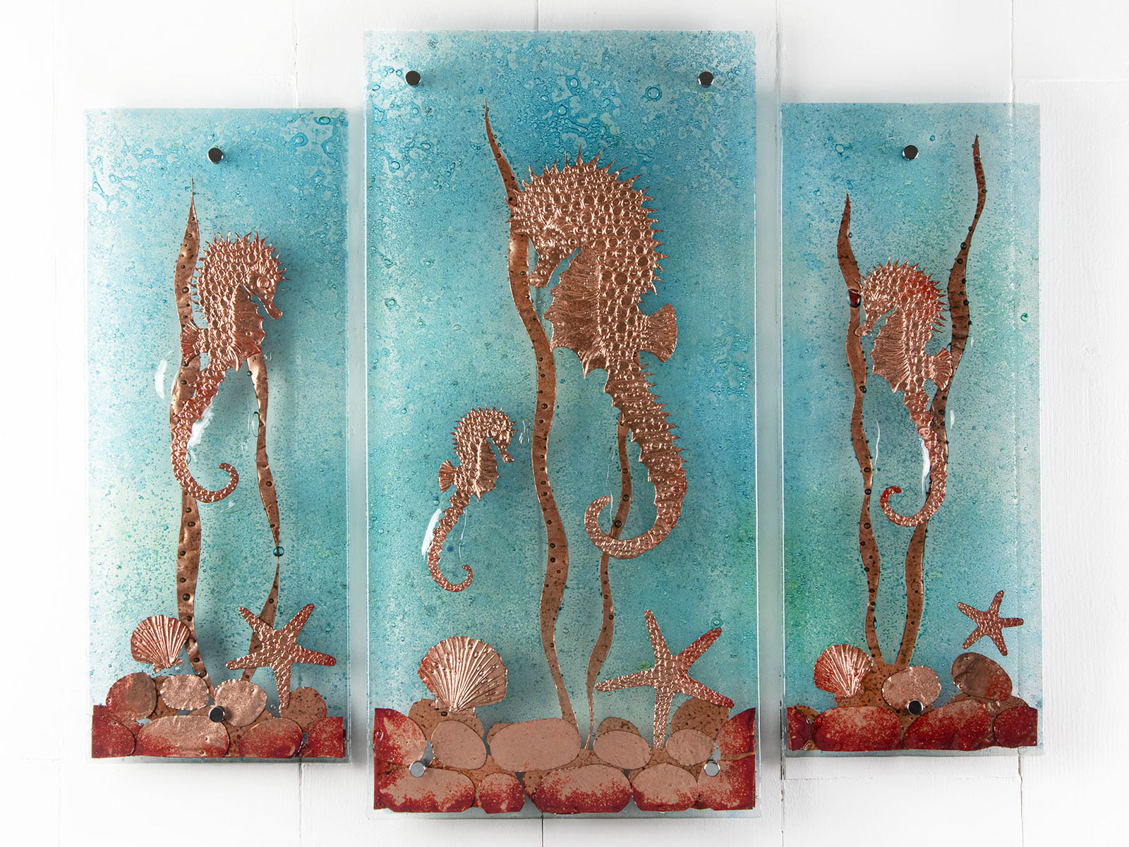 Fused glass staggered triptych, with hand-etched copper seahorses and ocean flora and an ocean blue background. 