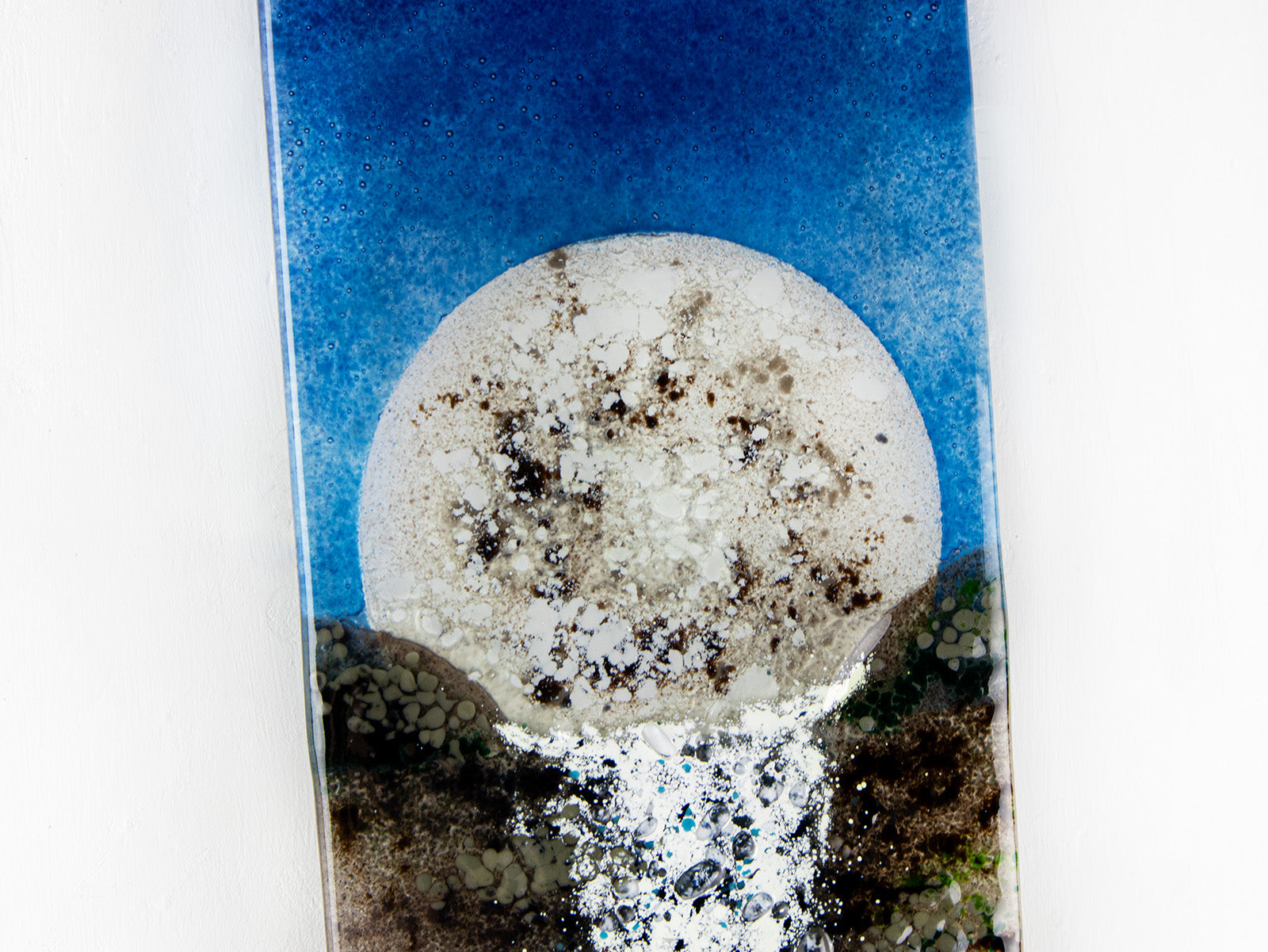 A close up of a fused glass wall panel featuring a rising full moon and a rushing waterfall. The design includes an organic colour-way and texture. 