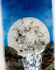 A close up of a fused glass wall panel featuring a rising full moon and a rushing waterfall. The design includes an organic colour-way and texture. 
