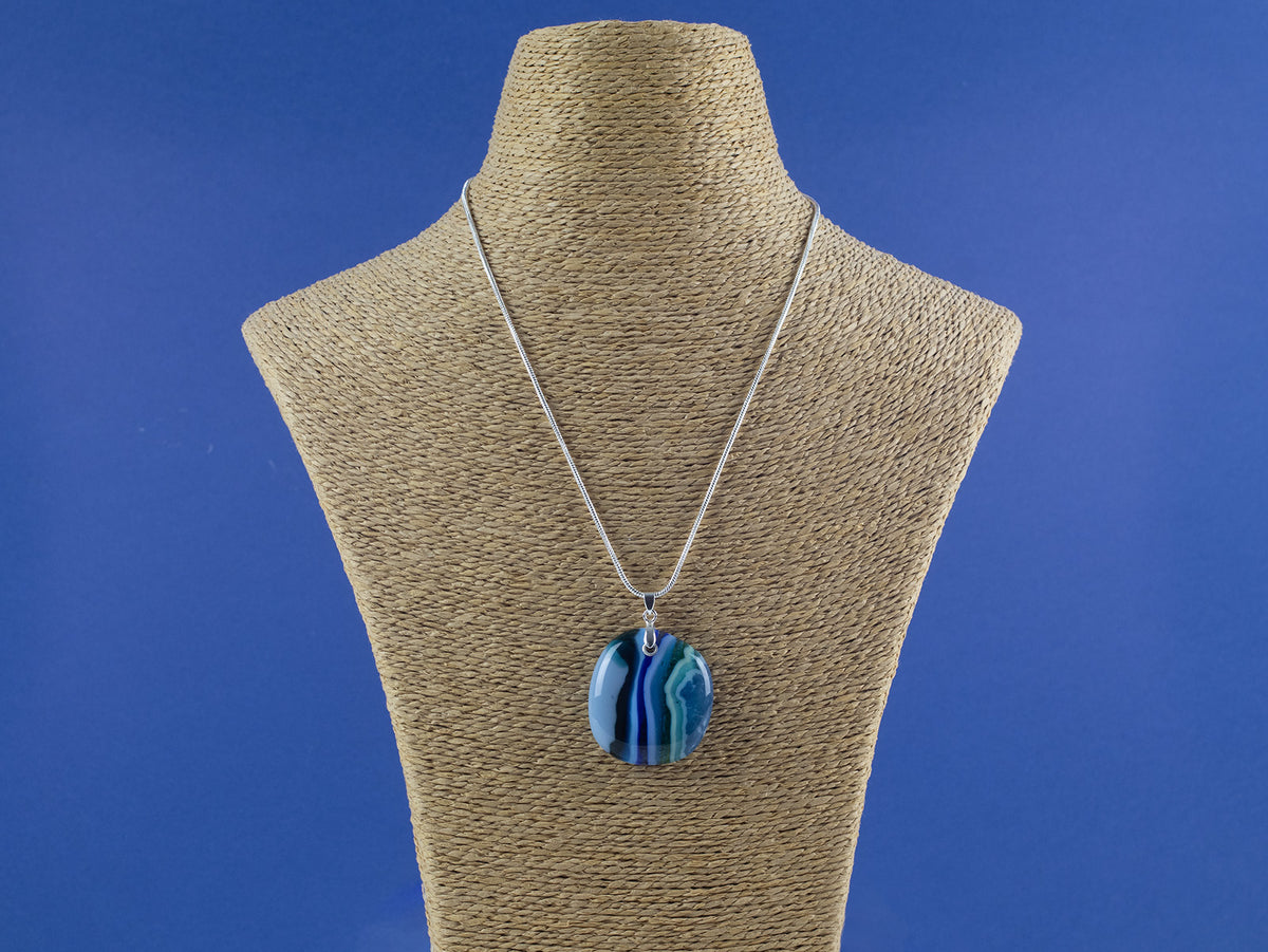 An artisan fused glass pendant necklace handcrafted in rich blues. Finished with a sterling silver chain and fittings, seen on a mannequin. 