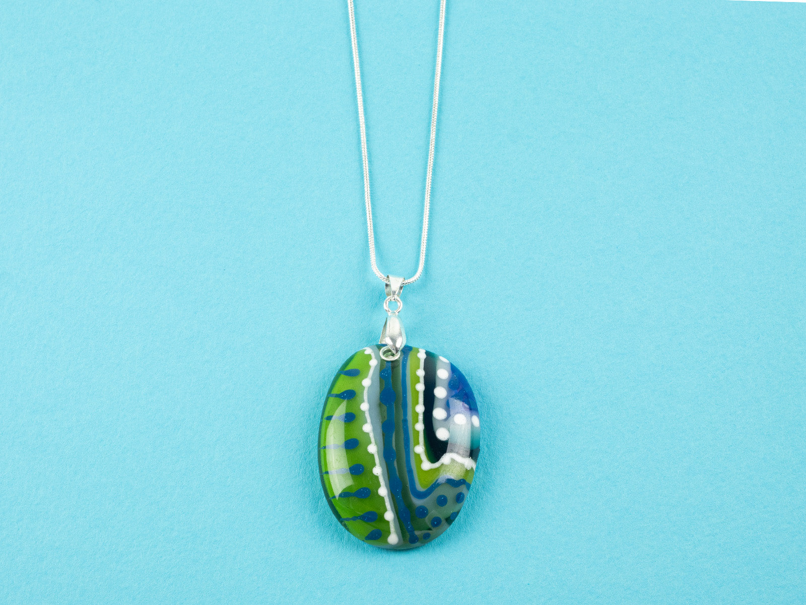 Fused glass pendant necklace, with hand-painted dots and swirls, in an ocean blue and green colour-way. Pendant is hung on a sterling silver chain. 
