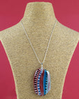 An extra large fused glass pendant necklace, handmade in rosey red and coastal blue hues, with hand-painted patterns and hung on a sterling silver chain 