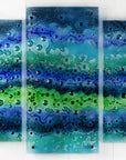A fused glass staggered triptych featuring an ocean inspired design, with a blend of coastal blues and sea greens, handmade with organic bubbled texture. 