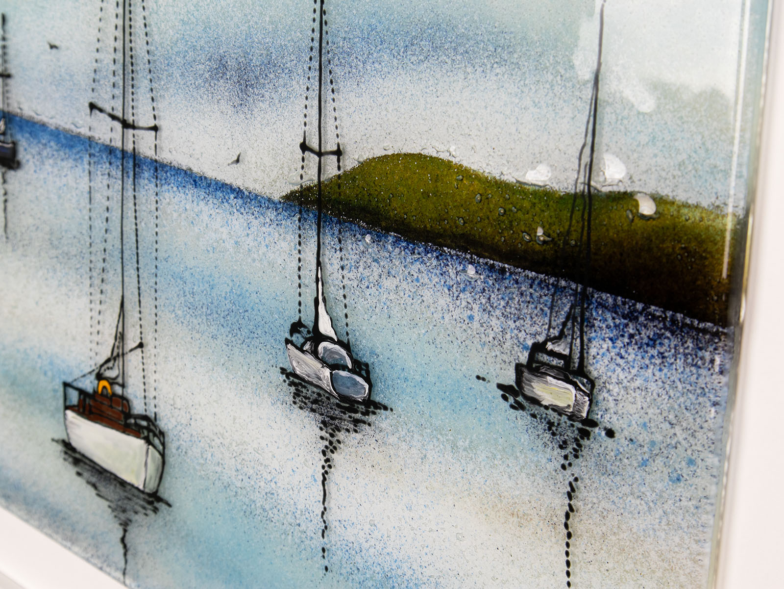 Details on a fused glass art frame featuring hand-painted sailing boats entering a harbour with soaring birds in a soft coastal colour-way. 