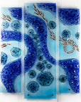 A fused glass staggered triptych wall display, handmade in bright ocean blues and aquas, in a coastal rock-pool design, featuring copper fish. 