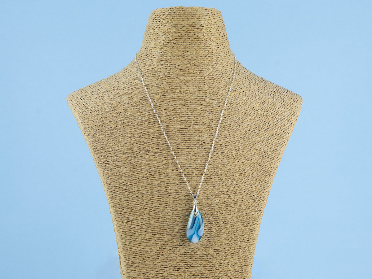 A fused glass pendant necklace, handmade in aqua blue hues, hung on a sterling silver chain. 