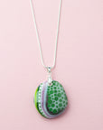 A fused glass pendant necklace, handmade in sea greens and blushed pinks, with hand-painted patterns, hung on a sterling silver chain. 