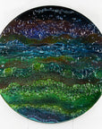 A round textured glass wall art piece featuring an abstract design with wavy organic hues.