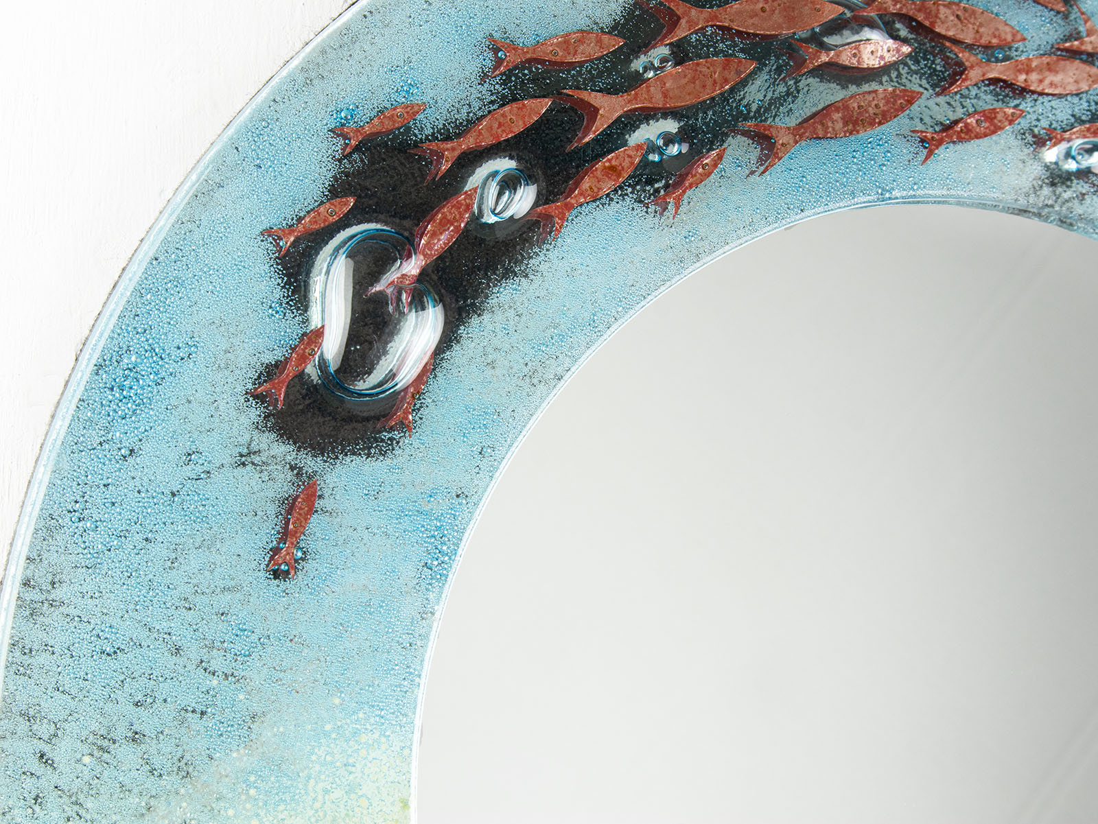 Close up of fused glass round mirror with ocean inspired design and copper fish detailing. Handmade, bespoke wall art. 