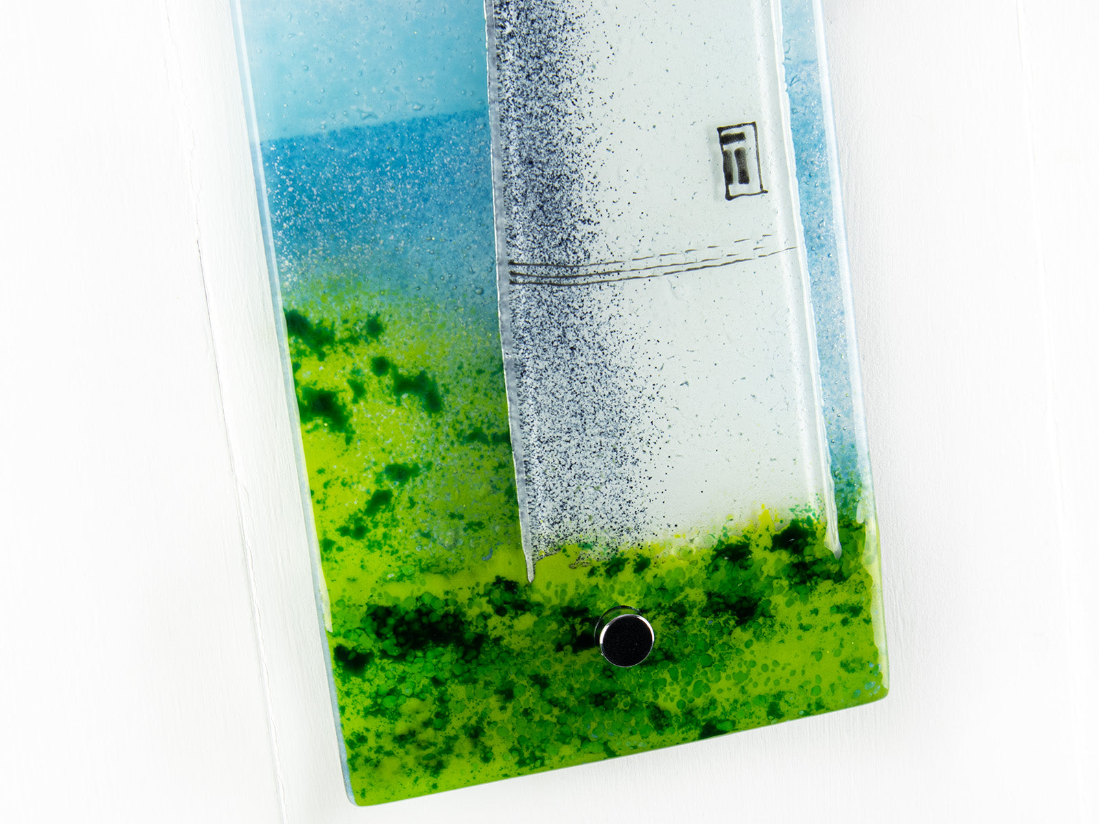 Detailing of a fused glass wall panel, featuring a lighthouse design on the cliff, inspired by Cornish coastline. 