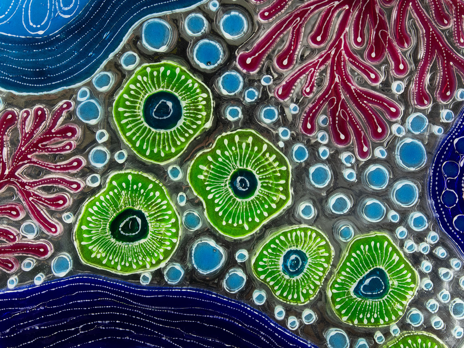 Close up of fused glass round wall panel with hand painted design of a coral reef. Organic and vibrant ocean colours. 