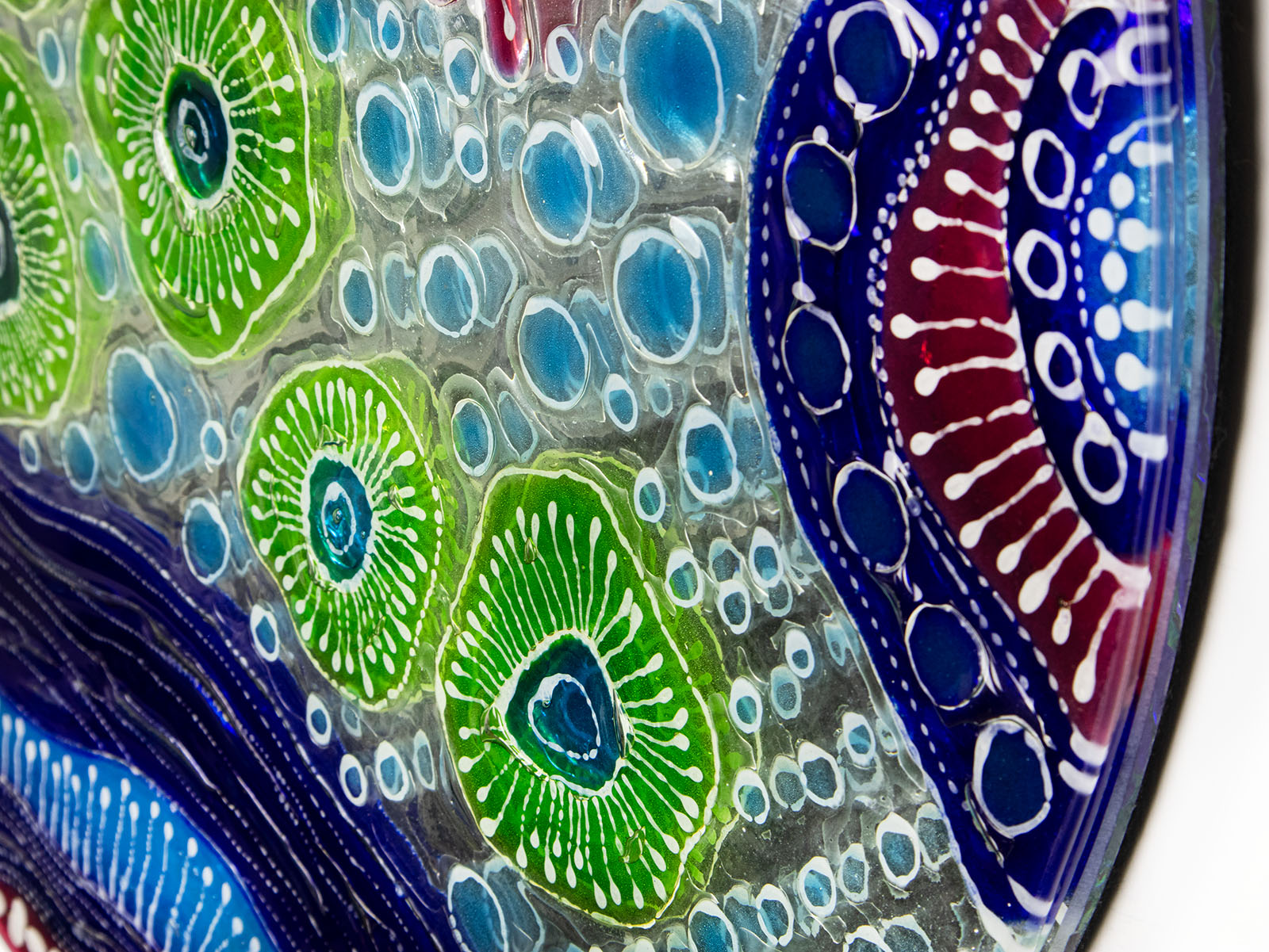 Close up of fused glass round wall panel with hand painted design of a coral reef. Organic and vibrant ocean colours. 
