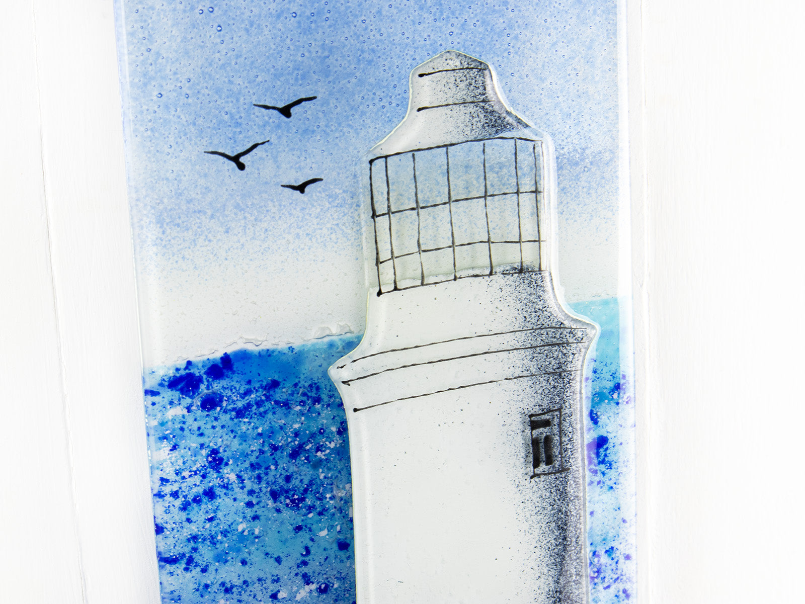 Close up of fused glass wall panel with lighthouse design and soaring seagulls. Handmade made in Cornish studio in coastal colours.