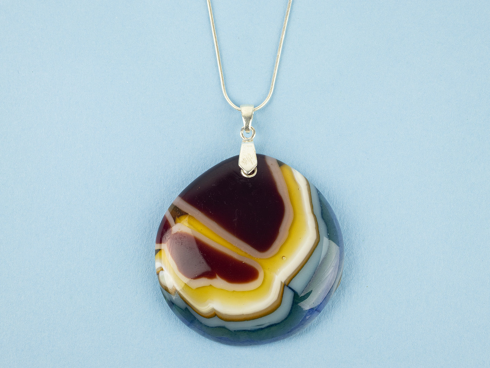 Close up of fused glass extra large pendant necklace, handmade in ruby reds and marine blues. Stunning jewellery with sterling silver chain. 