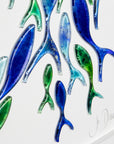 Close up of signed signature and fish individually hand-cut in marine blues on white art frame. An ocean inspired piece of wall art. 