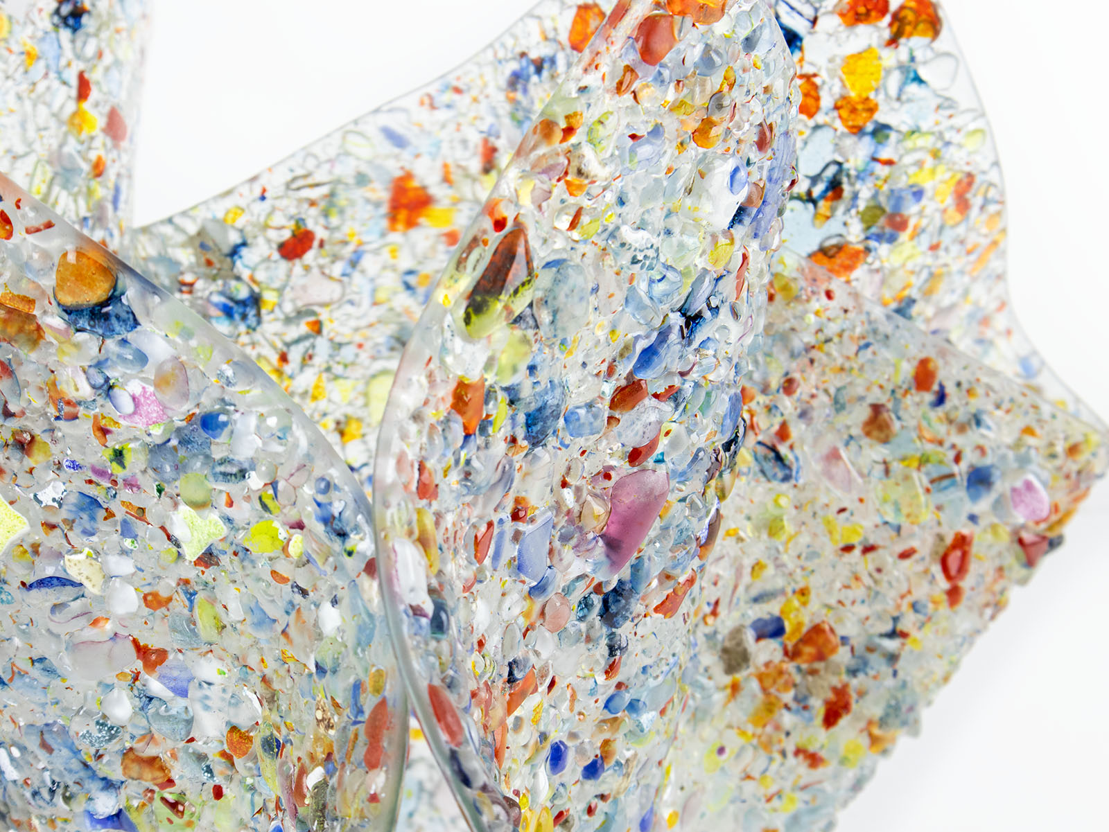 Close up of a fused glass extra large fold form vase, made from multi coloured, recycled glass frit. 