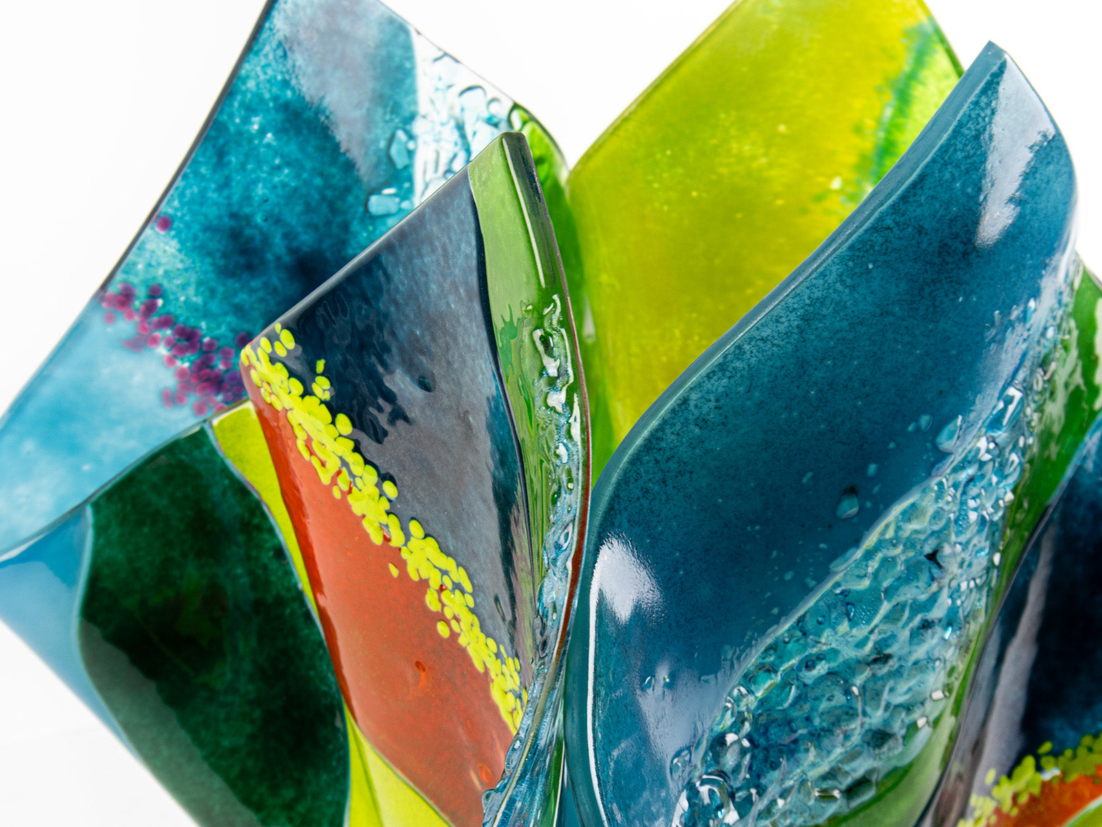Close up of  fused glass fold form vase, with bright greens and textural detailing. 