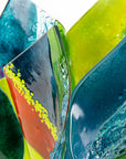 Close up of  fused glass fold form vase, with bright greens and textural detailing. 