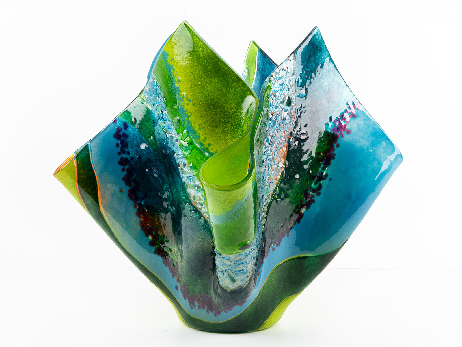 Fourth image of fused glass fold form vase, with bright greens and textural detailing. 