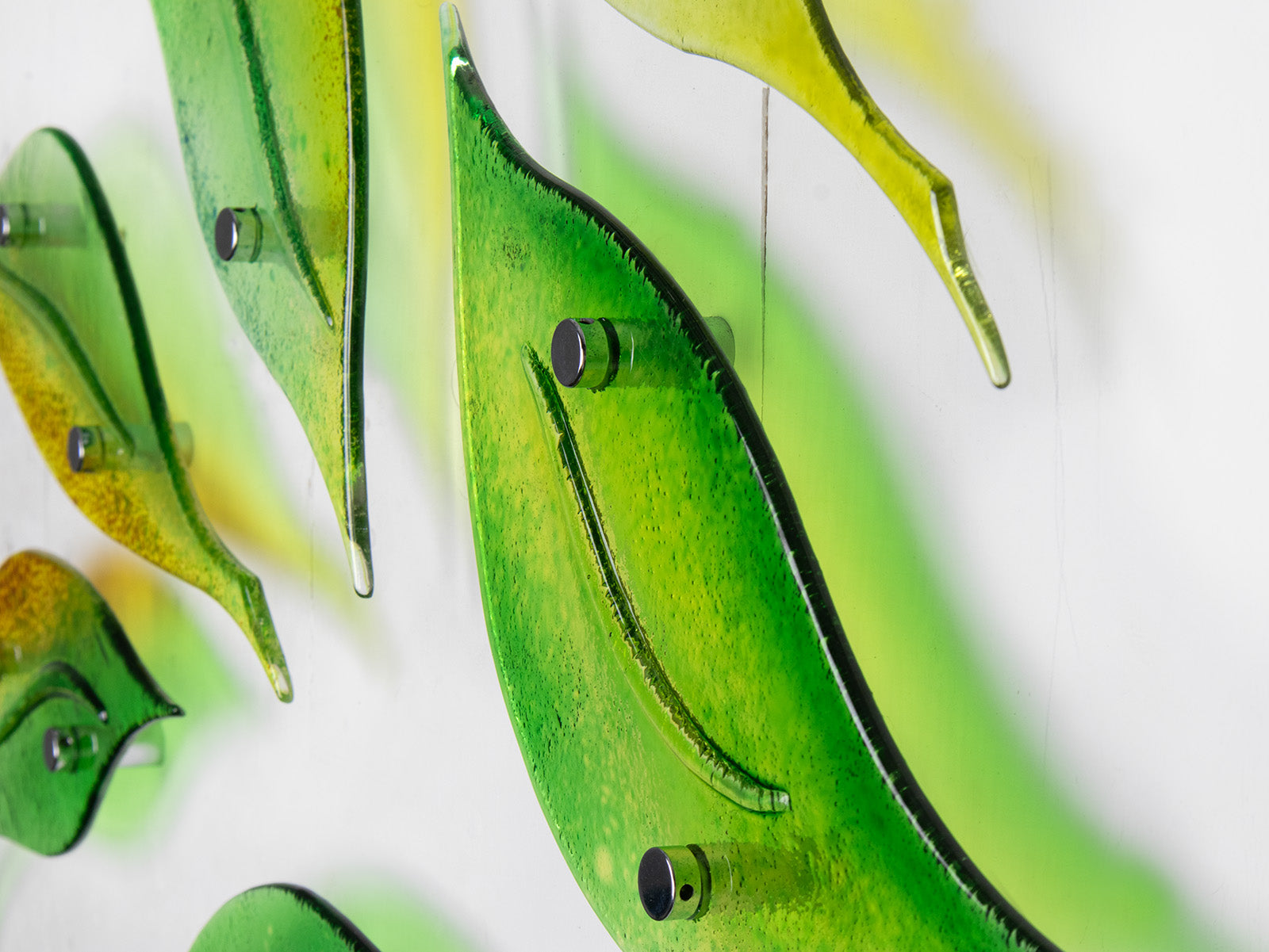 Close up of fused glass wall art display featuring individual spring leaves in vibrant colours. 