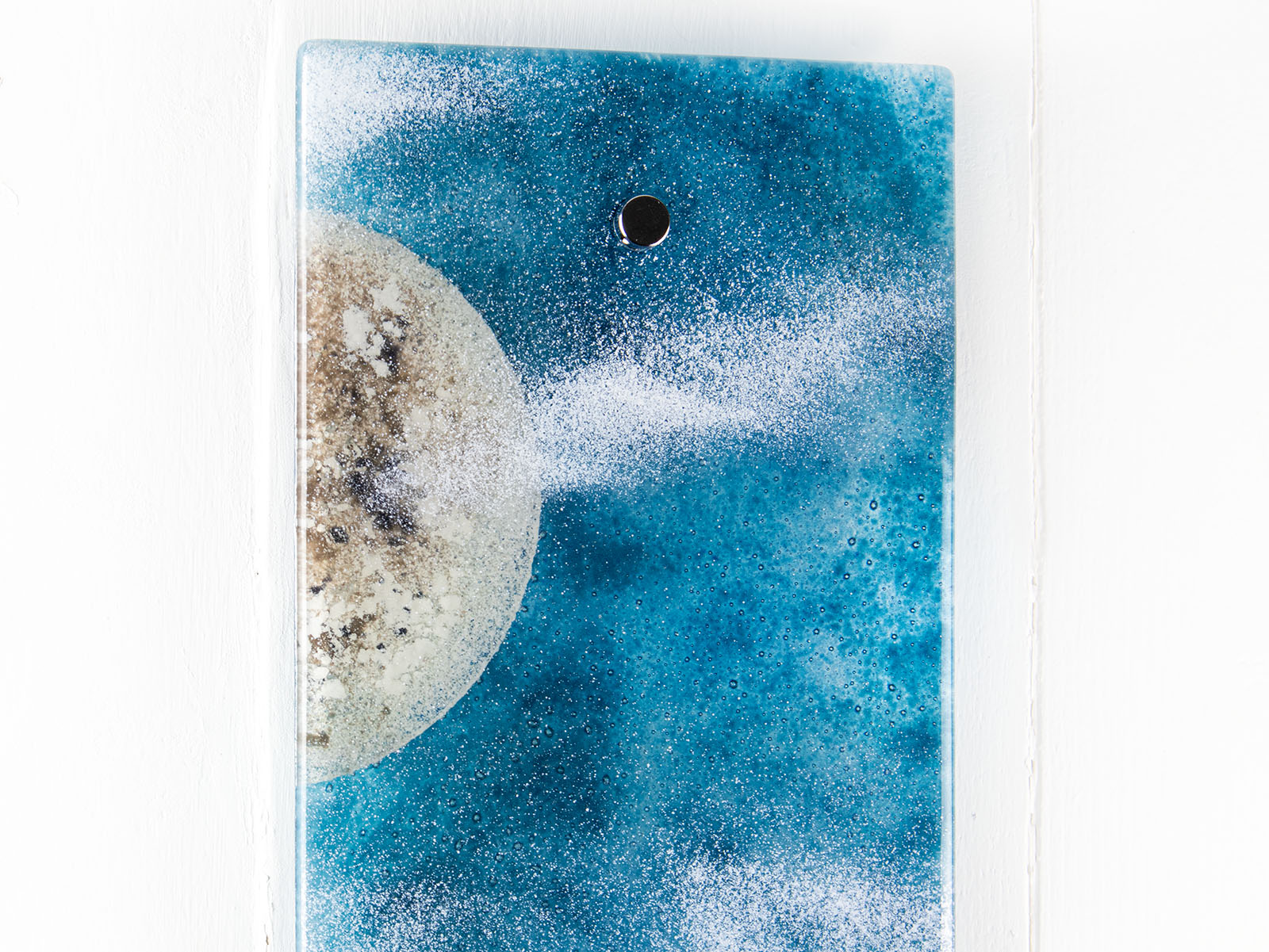 Details of fused glass wall panel featuring a Cornish lighthouse design with a teal blue background and full moon design. 